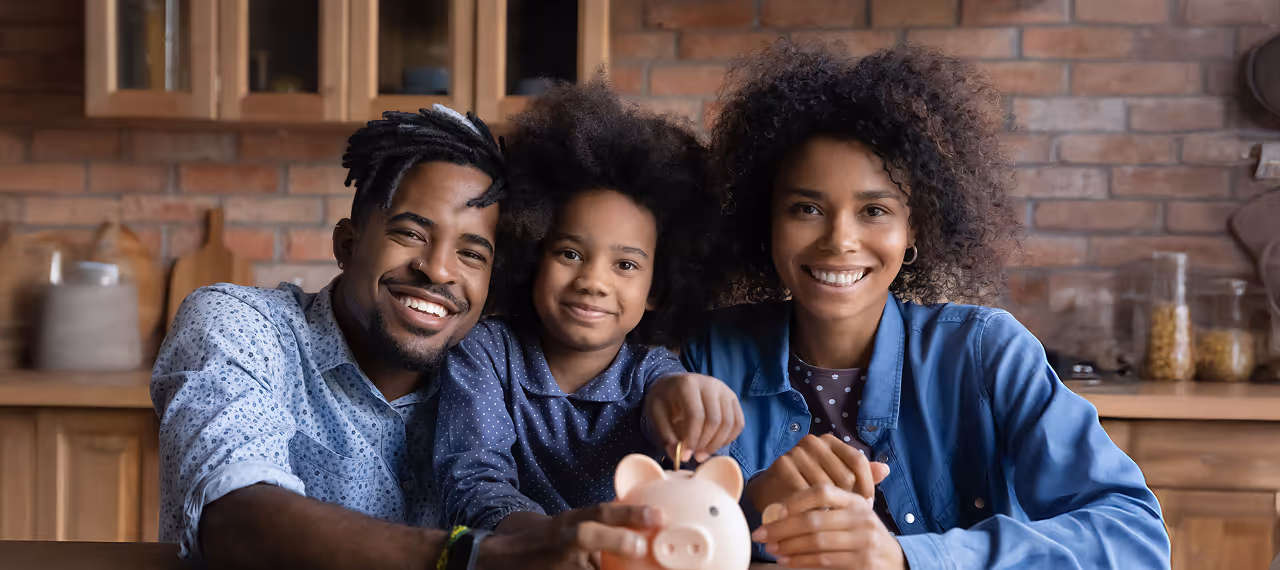 Smiling family of three holding a piggy bank together in a cozy kitchen.